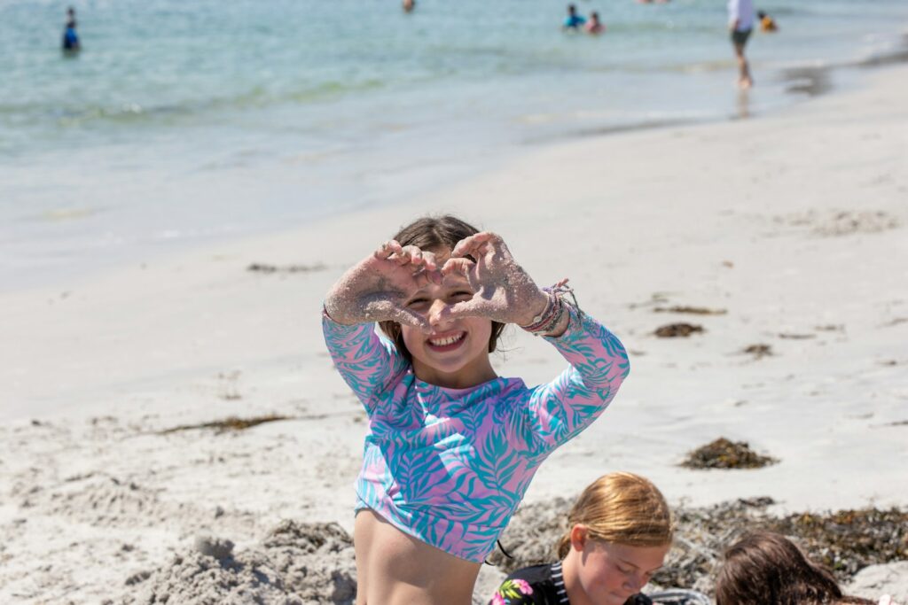 a young girl sitting on a beach next to another young girl